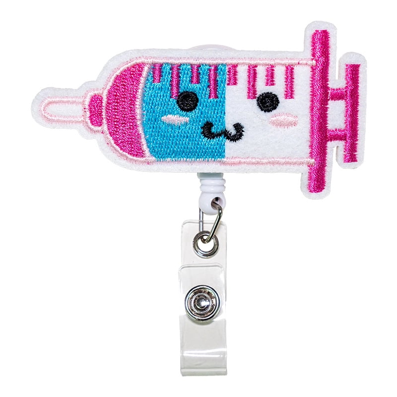 Porta carnet con forma de inyector, de color fucsia, blanco y azul, con borde rosado cosido. Tipo yoyo retráctil. Se conecta mediante un gancho metálico triangular unido a un aro metálico. Desde este aro se extiende un adaptador de color blanco con broche. Haga clic para ampliar la imagen
