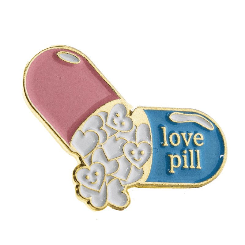Pin Capsula de colores GMD, con reborde dorado; un extremo rosado con detalle en blanco y el otro azul con detalle en blanco; texto “love pill” en dorado; en el centro, cápsulas en forma de corazón sobre fondo blanco, algunas sonrientes.. Haga clic para ampliar la imagen