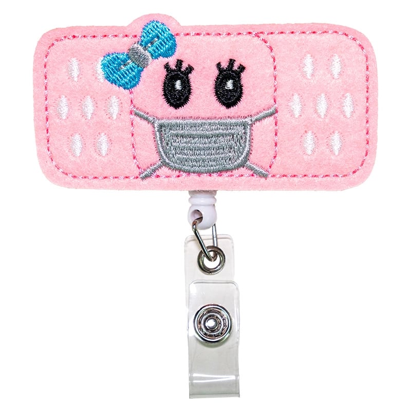 Porta carnet en forma de cura, de color rosado, blanco, azul y gris, con borde rosado cosido. Tipo yoyo retráctil. Se conecta mediante un gancho metálico triangular unido a un aro metálico. Desde este aro se extiende un adaptador de color blanco con broch. Haga clic para ampliar la imagen