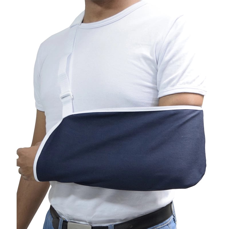 Cabestrillo adulto color azul profundo con reborde blanco, puesto en el brazo izquierdo de un hombre. Con correa de soporte, ajustador en el extremo derecho y almohadilla protectora blanca en la parte superior derecha.. Haga clic para ampliar la imagen