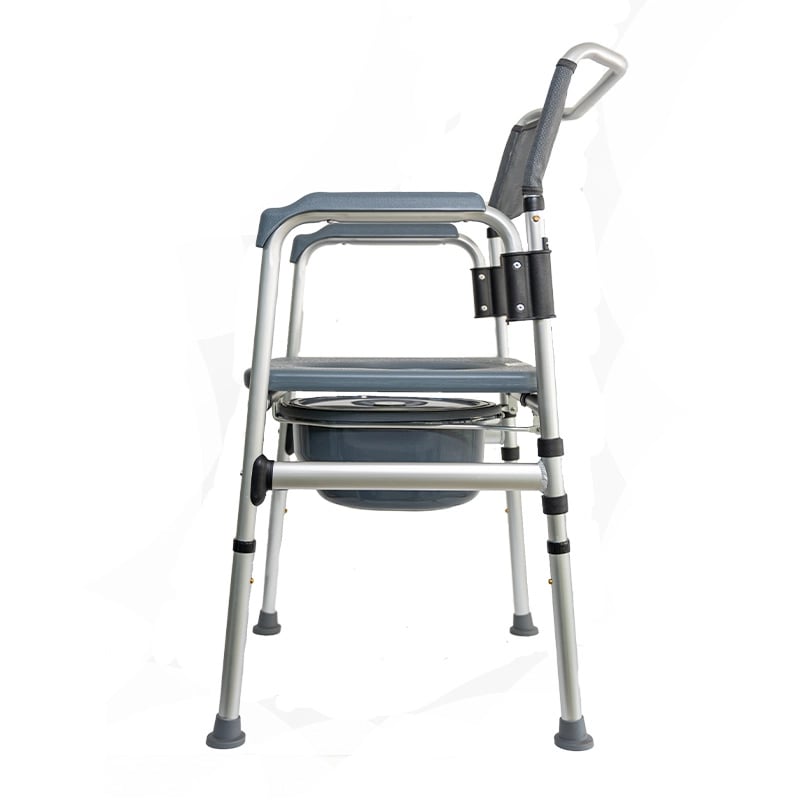 Comodo sanitario en aluminio anodizado, vista lateral izquierda, con estructura metálica de color plateado. Espaldar en malla de color gris y apoyabrazos acolchados de color gris. En el centro cuenta con asiento de color gris con apertura central tipo ino. Haga clic para ampliar la imagen