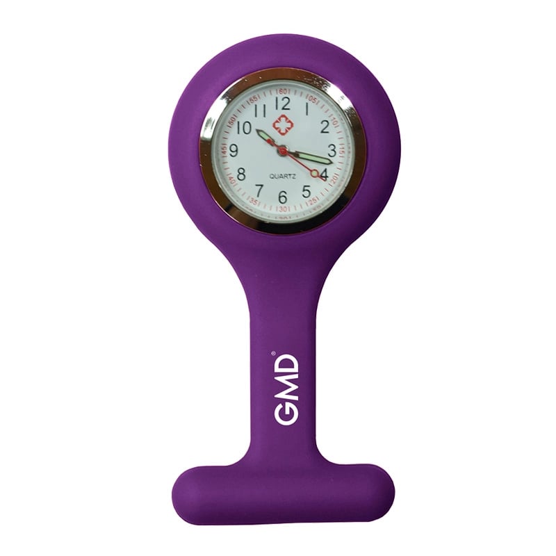 Reloj gmd color purpúra, con carcasa de silicona en forma de “T” y la marca “GMD”. Fondo blanco con números en la parte superior dispuestos en dos filas: primero números rojos y debajo números negros de mayor tamaño. En el centro tiene una pequeña cruz ro. Haga clic para ampliar la imagen