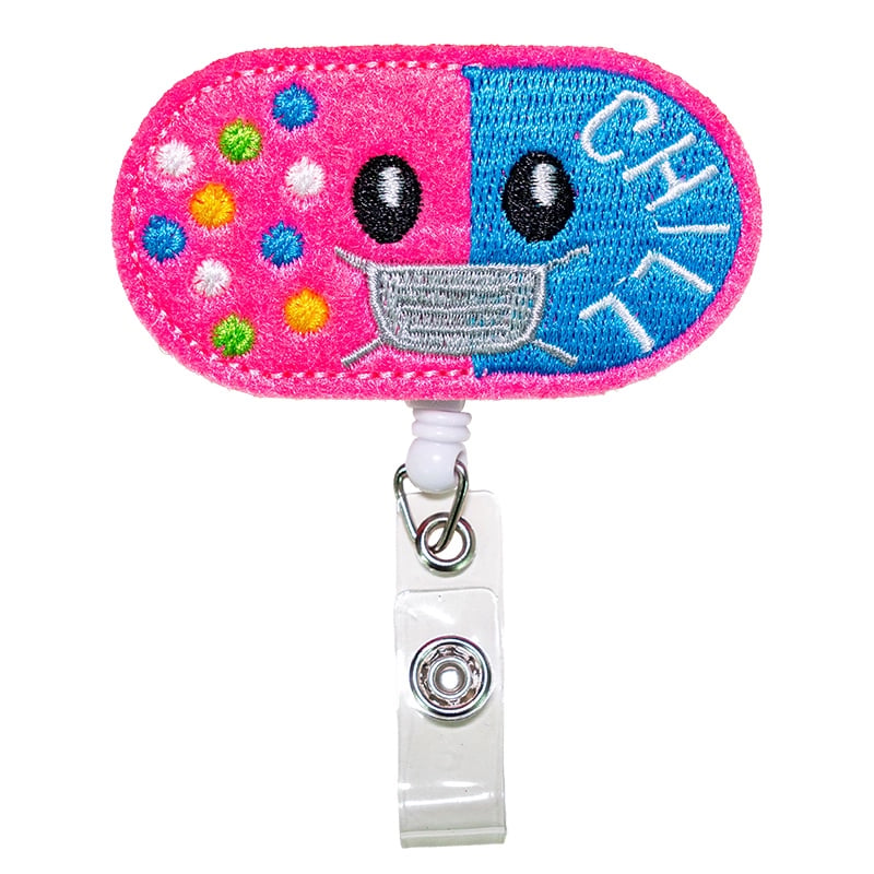 Porta carnet en forma de píldora, de color fucsia y azul, con borde rosado cosido. Tipo yoyo retráctil. Se conecta mediante un gancho metálico triangular unido a un aro metálico. Desde este aro se extiende un adaptador de color blanco con broche metálico . Haga clic para ampliar la imagen
